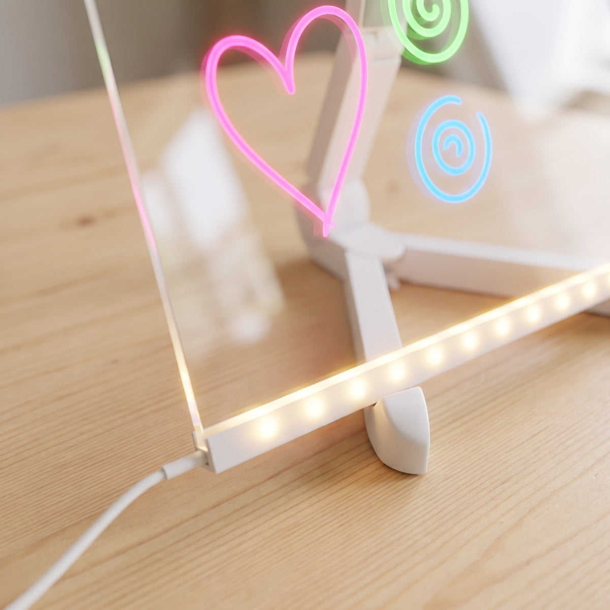 The glowing light bar along the bottom of the clear board up close, with the cable plugged in and a lit-up pink heart above.